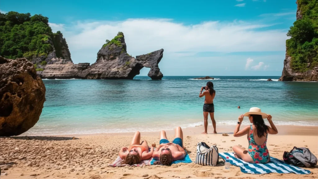 Tourists relaxing on the tropical sandy beach facing natural rock arch at Atuh Beach Nusa Penida